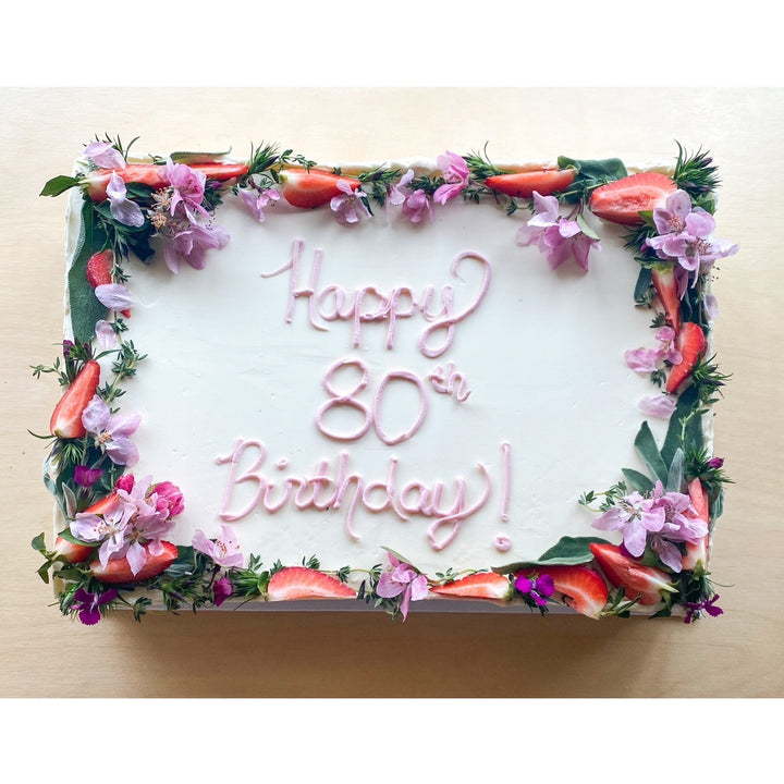 A sheet cake decorated with a floral border and the message "Happy 80th Birthday!" piped in pink buttercream.