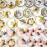 Dozens of wreath-shaped cookies decorated with colored glazes and pressed florals.