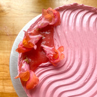 A close-up of wavy hot-pink buttercream, which run parallel to pools of rhubarb compote decorated with fresh snapdragon flowers.