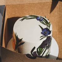 A cake decorated with a crescent of pressed flowers, sitting in a box