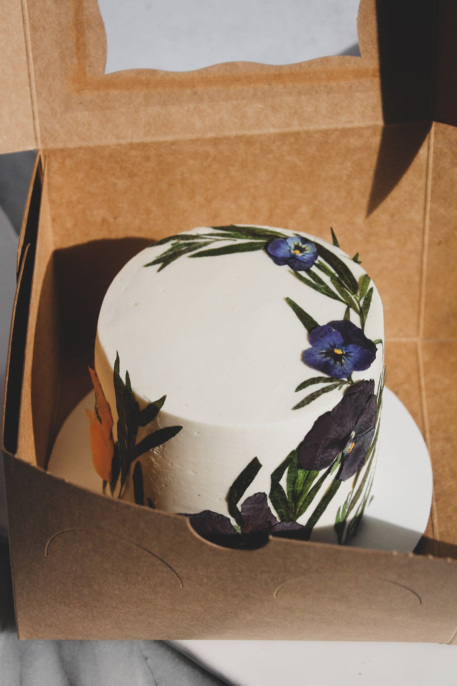 A cake decorated with a crescent of pressed flowers, sitting in a box