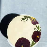 A top-down view of a cake covered in smooth white buttercream and a crescent of pressed flowers