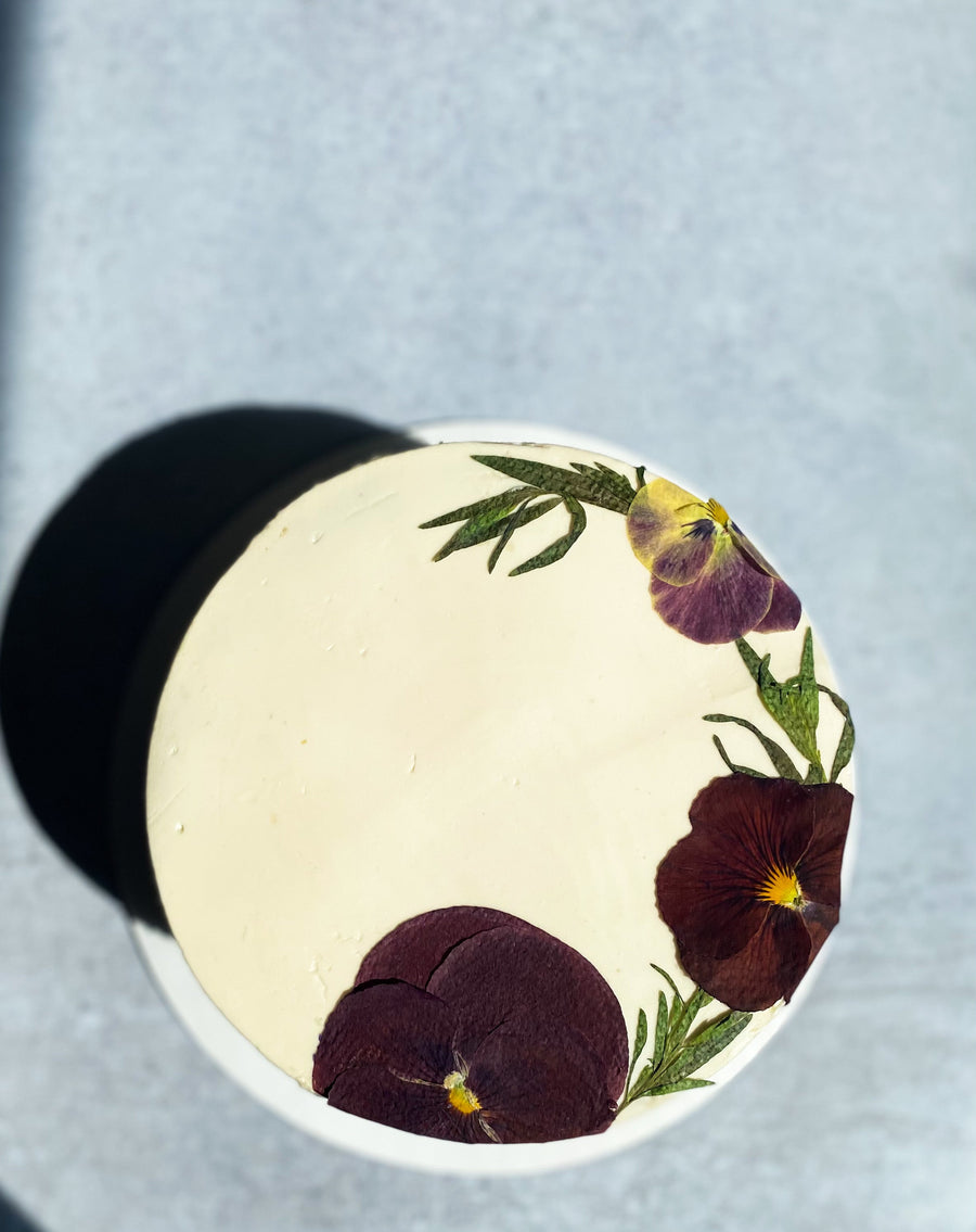 A top-down view of a cake covered in smooth white buttercream and a crescent of pressed flowers