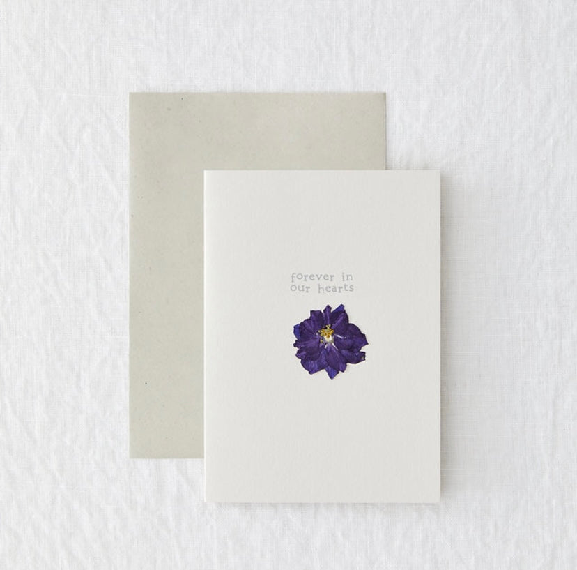A white card with a pressed flower. "forever in our hearts"