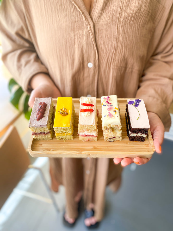 A woman holding a board with five cake slices, each a different flavor.