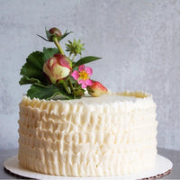 A round cake decorated with white buttercream ruffles along the sides and topped a bouquet of fresh flowers.