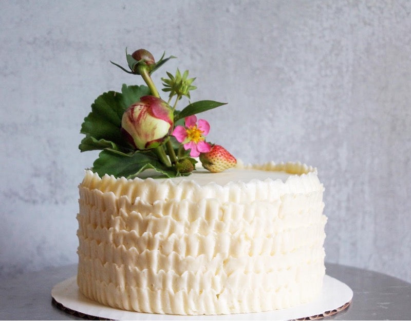 A round cake decorated with white buttercream ruffles along the sides and topped a bouquet of fresh flowers.