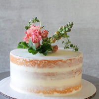 A round cake covered in a sheer layer of white buttercream and decorated with a bouquet of fresh flowers and greenery on top.