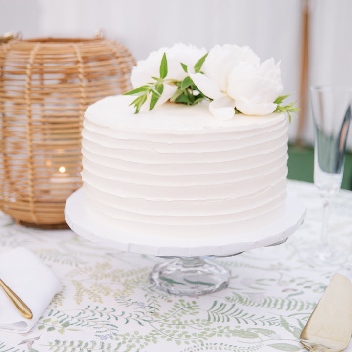 A tall round cake frosted with horizontally corrugated white buttercream and topped with a bouquet of white flowers.
