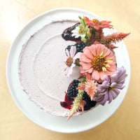 Top-down view of a round cake frosted with a sheer layer of purple buttercream and topped with a bouquet of flowers and blackberries.