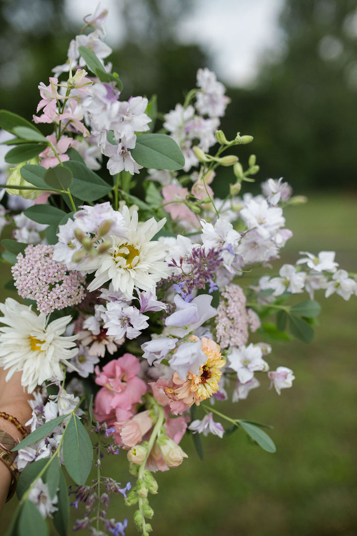 A bouquet of fresh, pastel-toned flowers. Colors include white, pink, yellow, and purple.