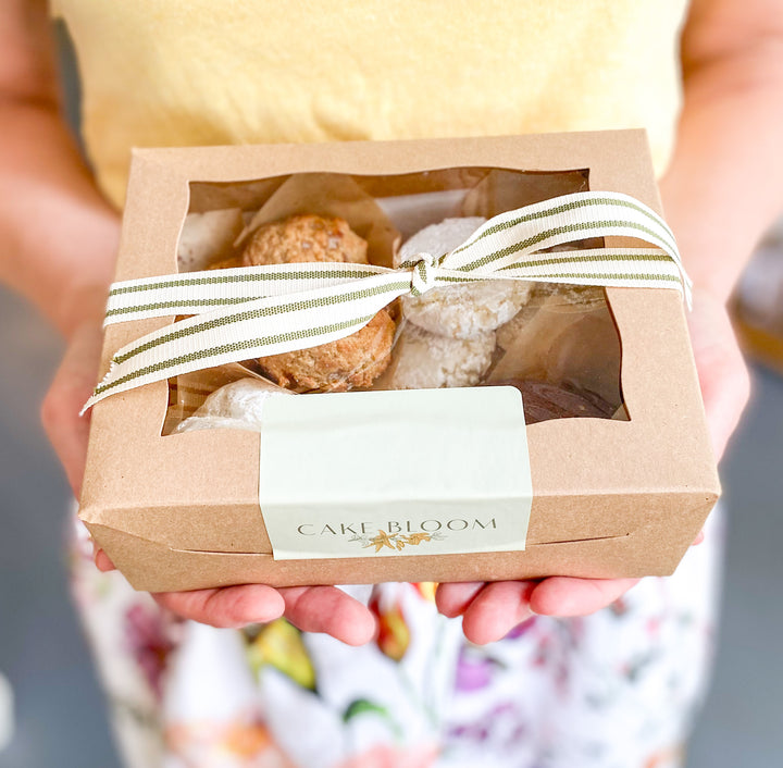 A person holding a box filled with cookies and wrapped with gift ribbon.