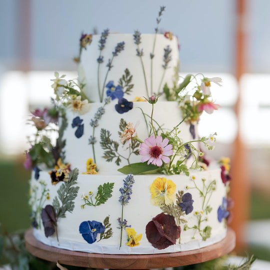 A three-tier wedding cake decorated with multi-color fresh and pressed flowers.