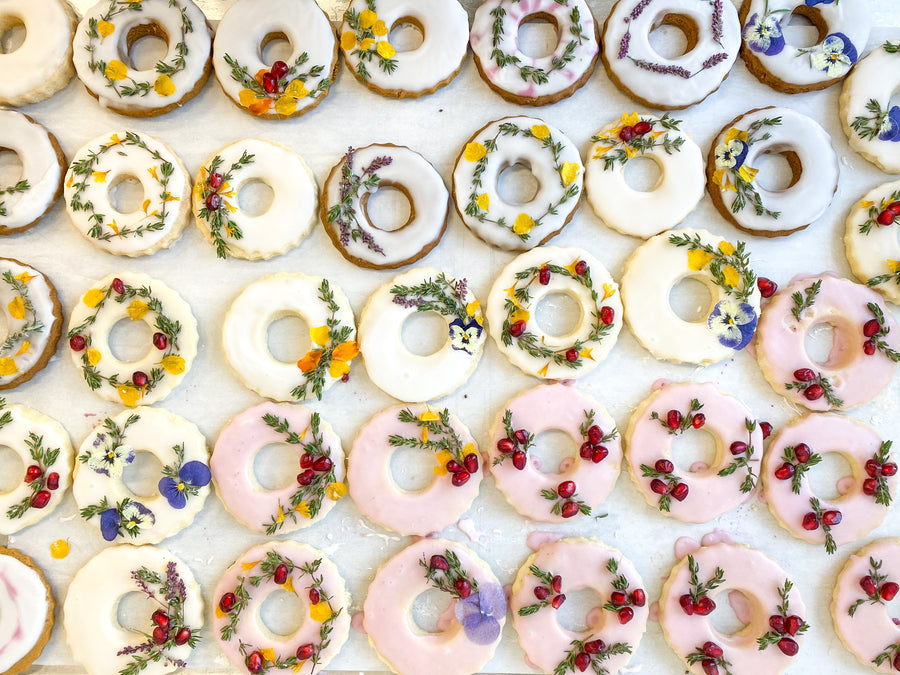 Dozens of wreath-shaped cookies decorated with colored glazes and pressed florals.
