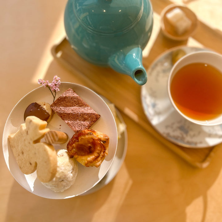 A small tea tower with an assortment of treats beside an antique teapot and cup of tea.