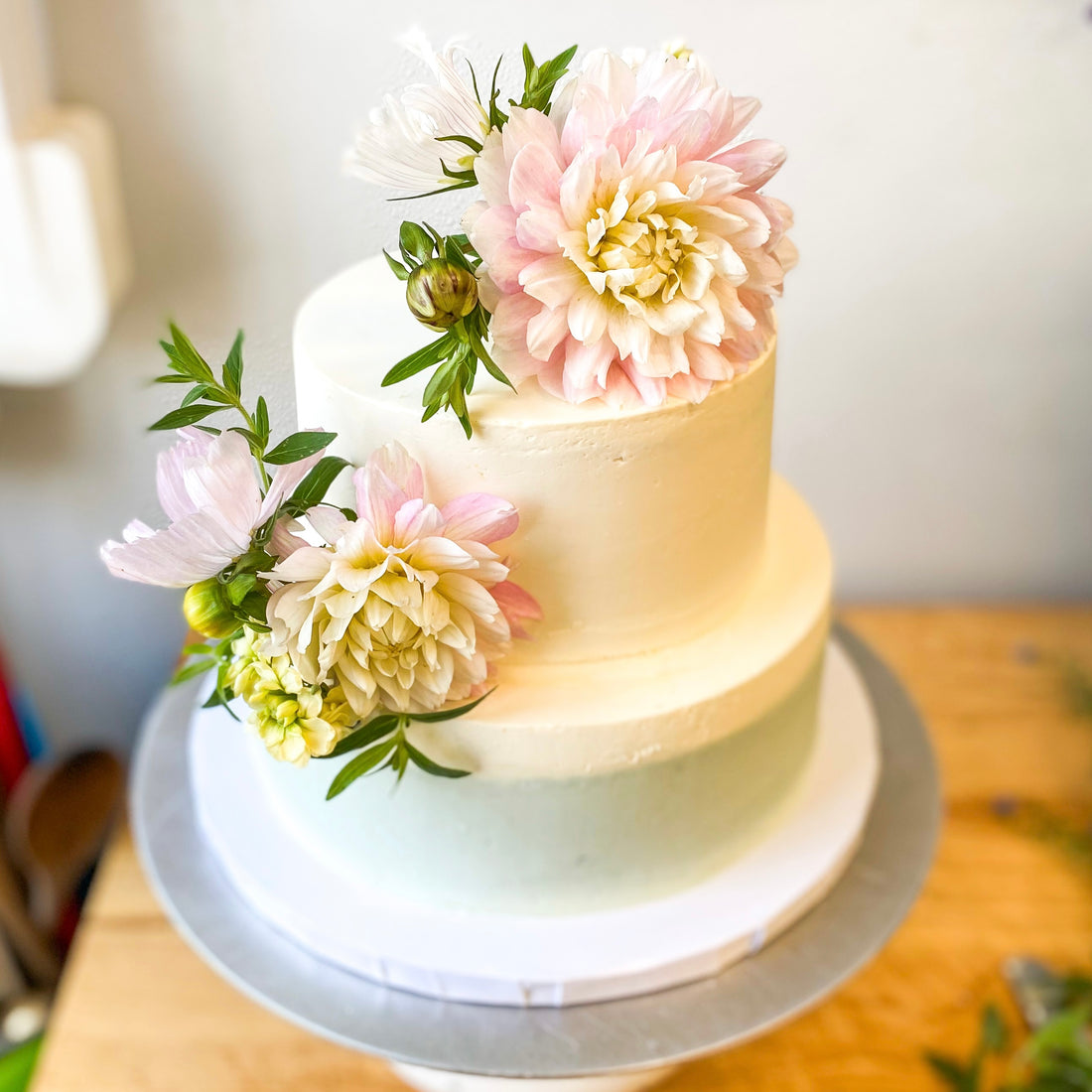 A two-tier cake decorated with two diagonal floral bouquets. The bottom half of the bottom tier is frosted with a defuse band of blue buttercream; the rest of the cake is white.