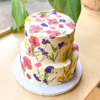A two-tier cake frosted with smooth, white buttercream and decorated with pressed flowers.