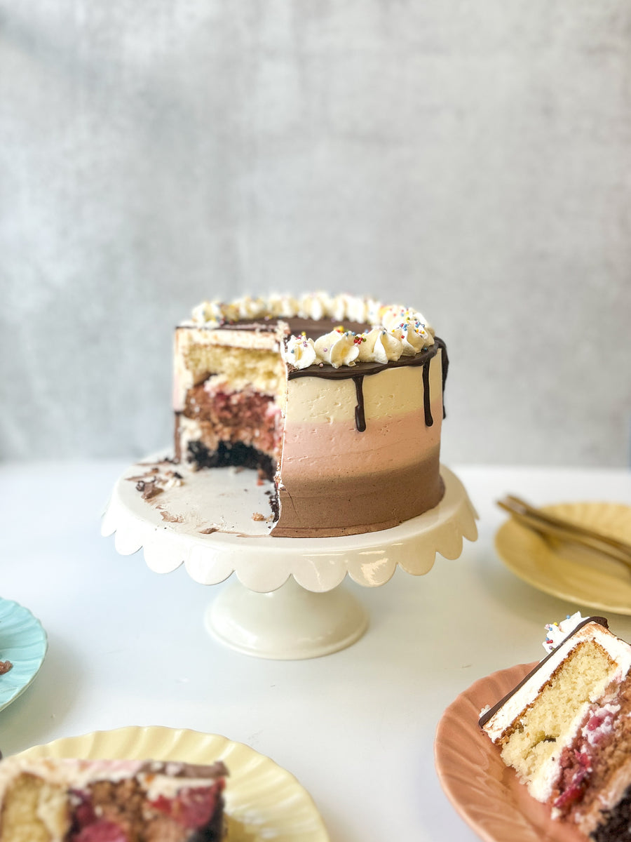 A round cake frosted with three bands of different flavors: vanilla, chocolate, and strawberry. The cake has been cut into, revealing the same layers of flavor inside the cake.