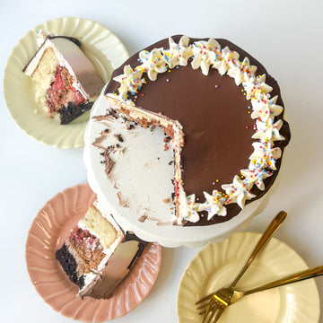 Top-down view of a round cake topped with chocolate ganache and decorated with a crown of whipped cream and rainbow sprinkles.