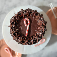 Top-down view of a chocolate cake decorated with a ganache rosette crown and a miniature candy cane.