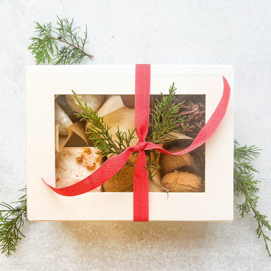 A white gift box containing two square cakes and a variety of cookies. The box is tied with a red ribbon.