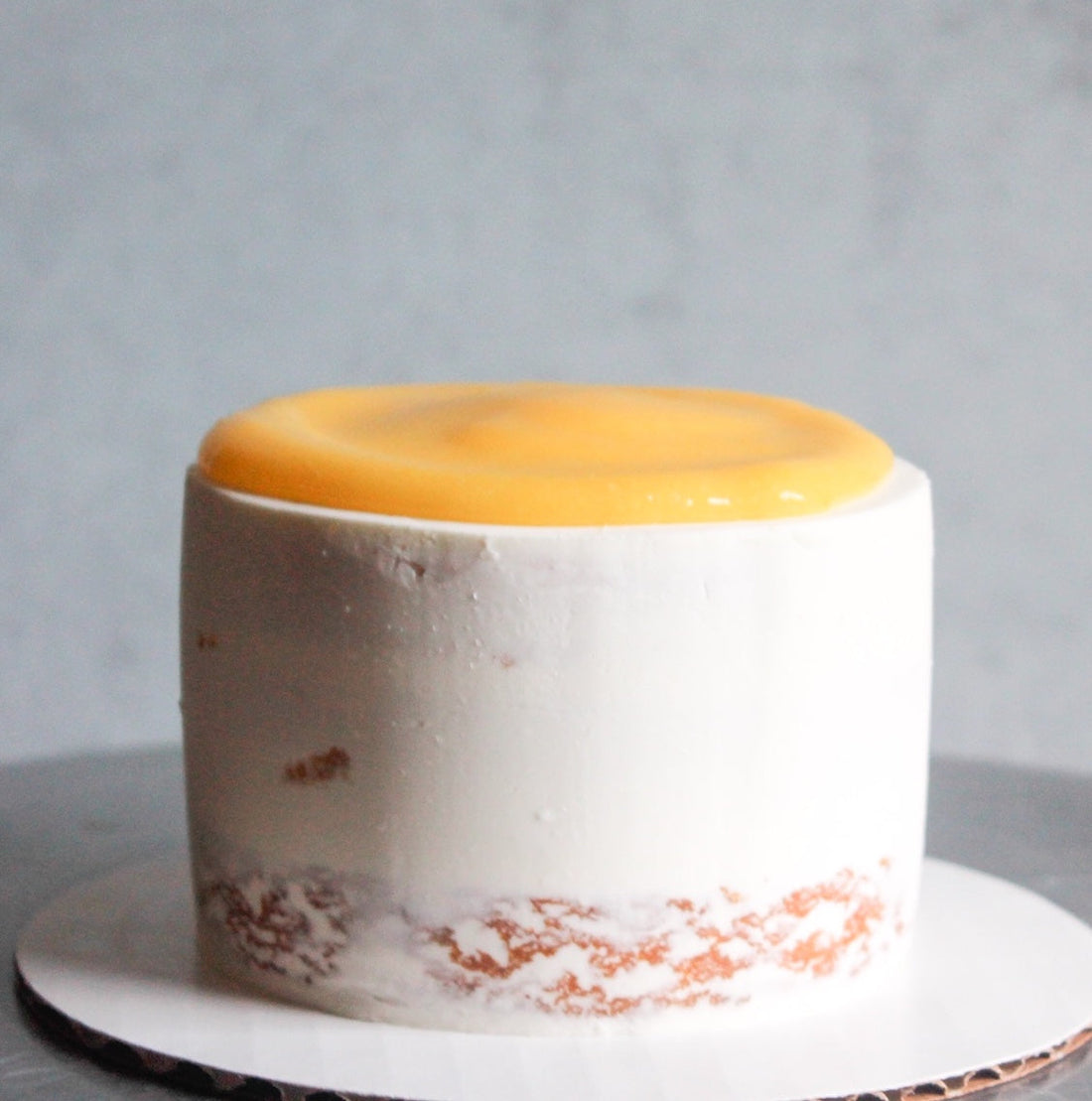 A round cake frosted in a sheer layer of white buttercream and topped with a pool of lemon curd.