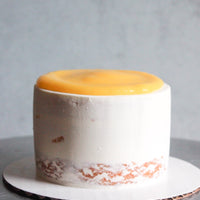 A round cake frosted in a sheer layer of white buttercream and topped with a pool of lemon curd.