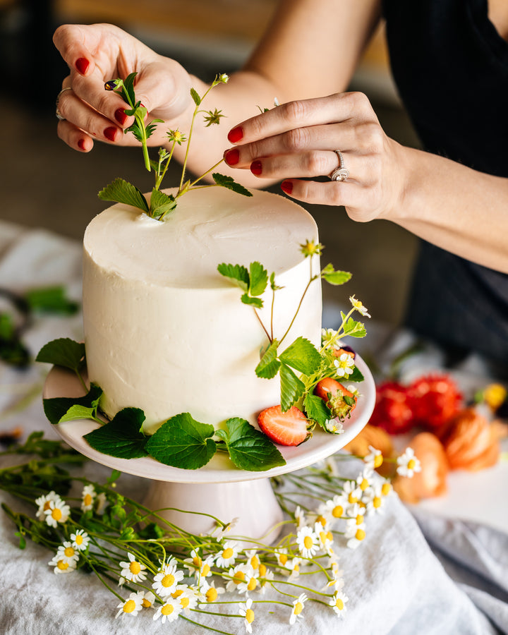 A person arranging floral decorations on a cake.