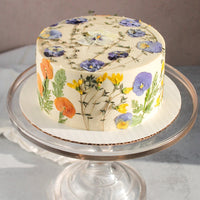 A cake frosted with smooth, white buttercream and decorated all over with pressed flowers.