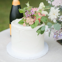 A tall round cake frosted with rustic white buttercream and and topped with a colorful floral bouquet.