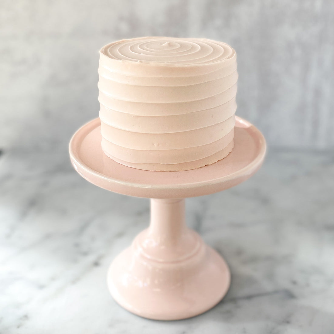 A round cake frosted in light pinked buttercream, which has been applied in a spiral pattern top to bottom.