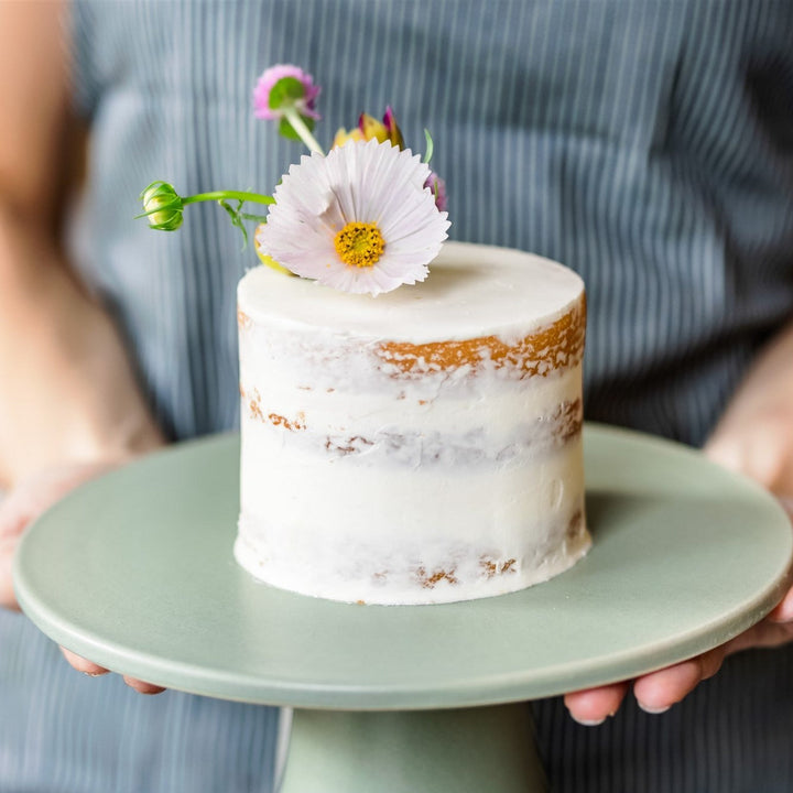 A round cake covered in a sheer layer of white buttercream and decorated with plume of fresh florals on top.