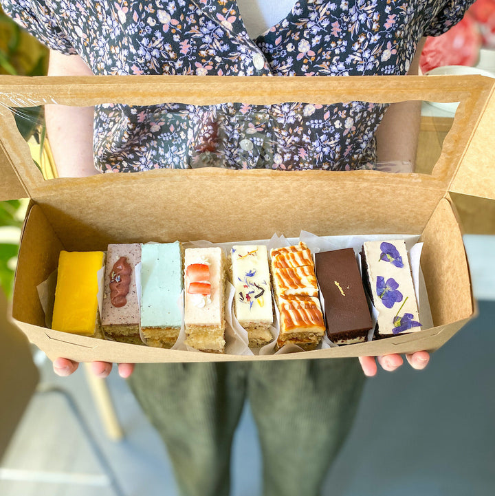 A Kraft box containing eight rectangular slices of cake, each a different flavor.