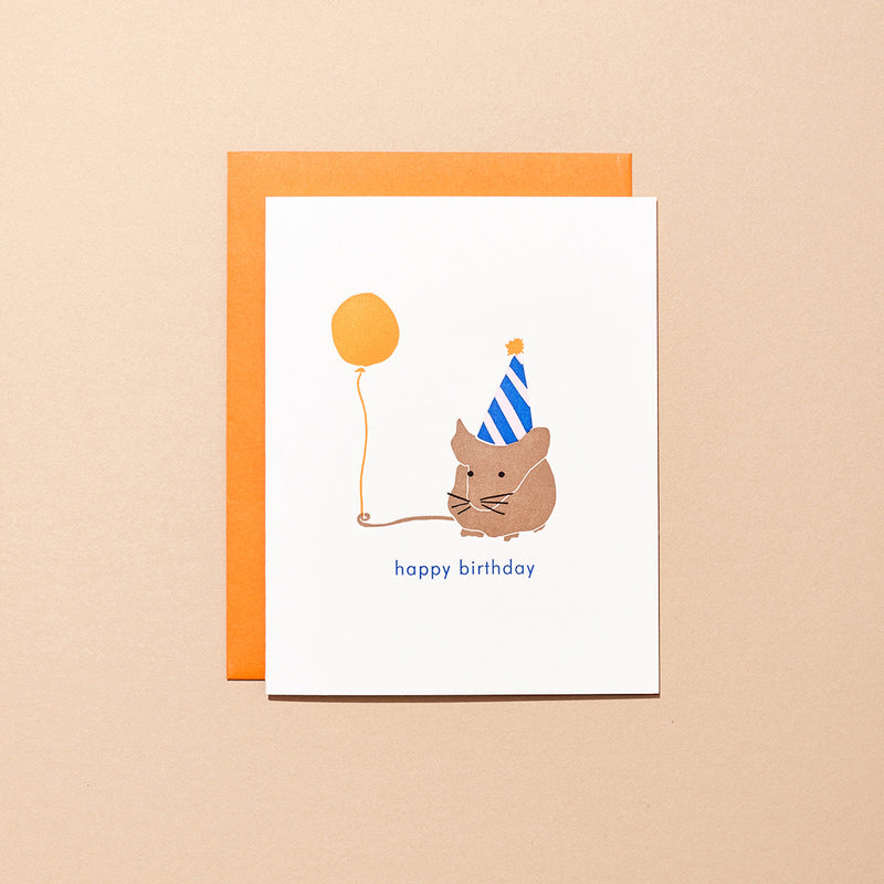 A letterpress card with a small mouse in a birthday with a balloon, beside the words "happy birthday". The card comes with an orange envelope.