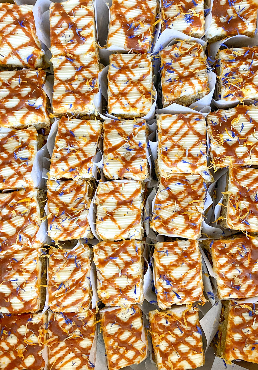 Top-down view of several square carrot cake slices, each wrapped in parchment paper.