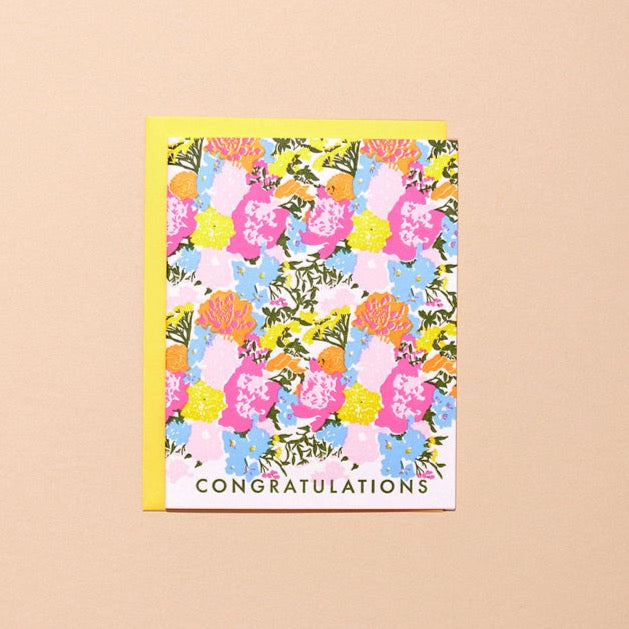 A card printed all over with a colorful flower pattern and the word "CONGRATULATIONS" at the bottom. The card comes with a yellow envelope.