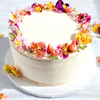 A round cake covered in a sheer layer of white buttercream and decorated with a crown of fresh flowers and sliced strawberries.