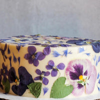 A cake frosted with smooth, white buttercream and decorated all over with pressed flowers.
