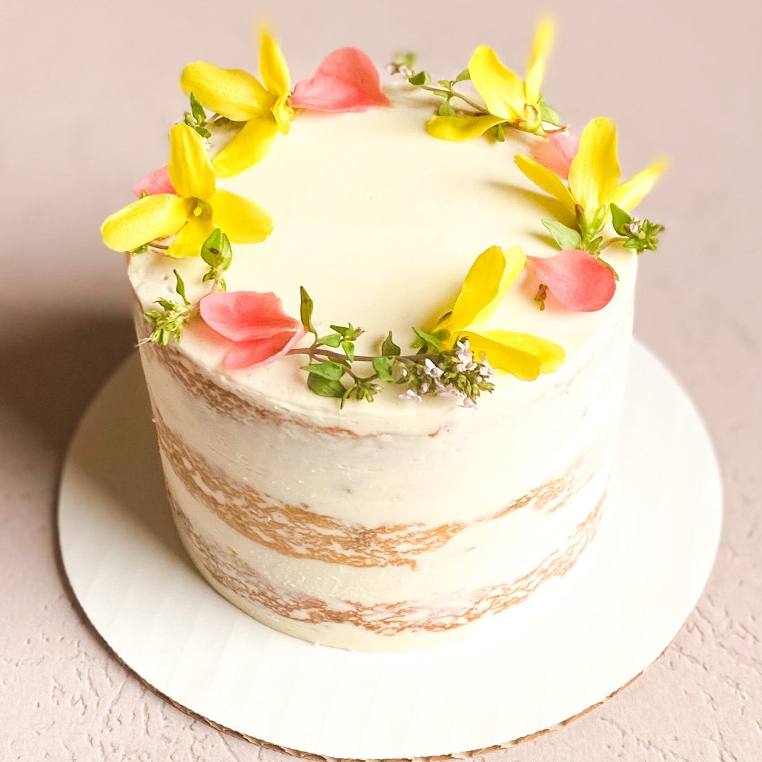 A round cake frosted in a sheer layer of white buttercream and decorated with a fresh floral crown.