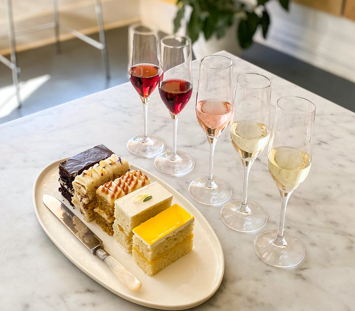A platter of five cake slices beside a flight of wine