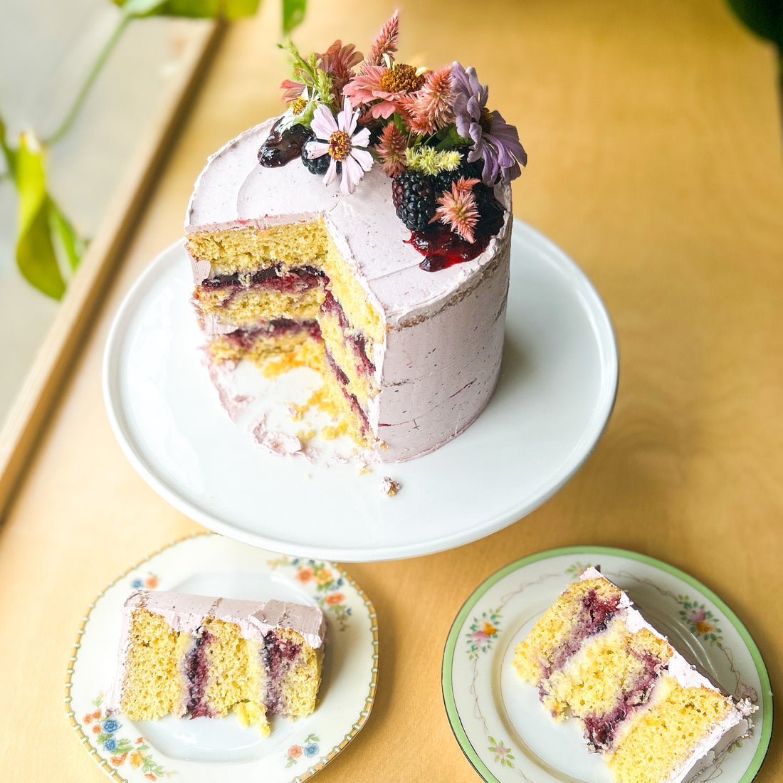 A cake frosted with purple buttercream, cut into slices to reveal layers of yellow cake, sweet corn cream, and blackberry jam.