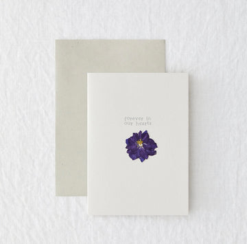 A white card with a pressed flower. "forever in our hearts"