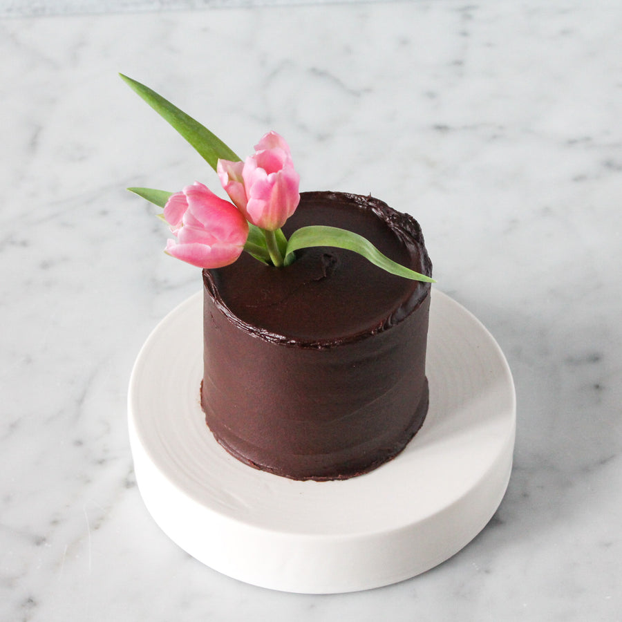 Top-down view of a small round cake covered in ganache and topped with a bouquet of pink tulips.