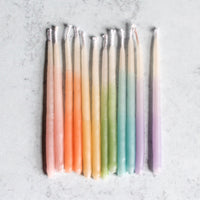 Twelve handmade wax candles, each a different color of the rainbow.