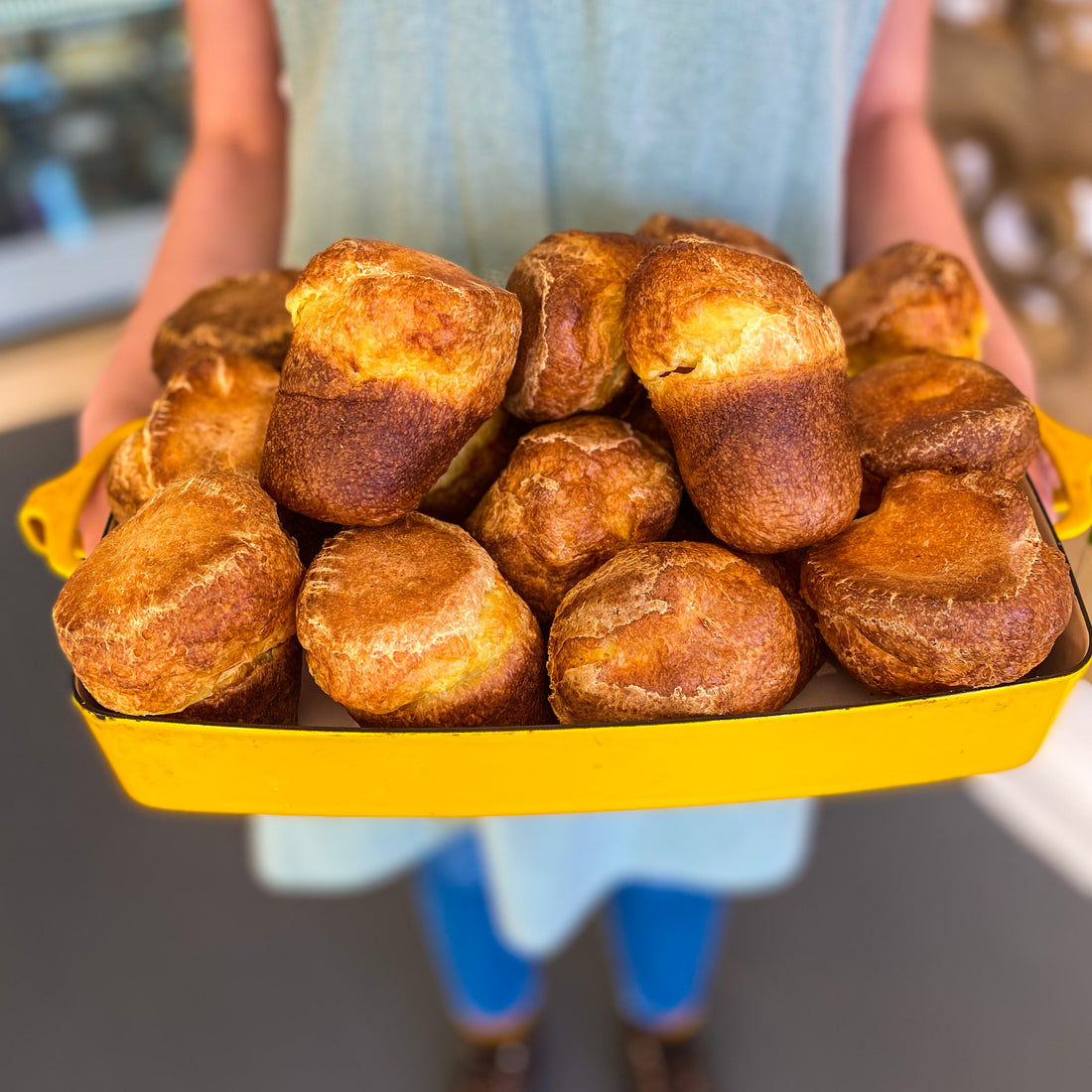 A person holding a dish containing dozens of fresh popovers.